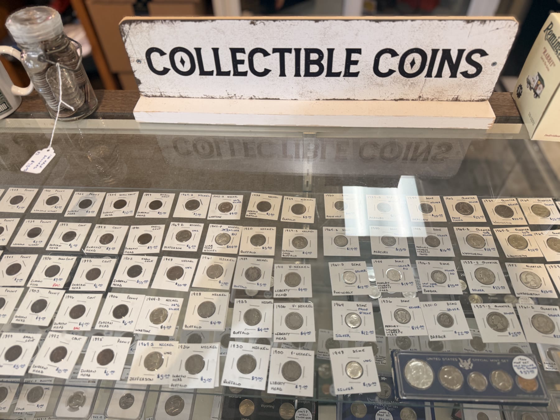Wooden 'Collectible Coins' sign over a glass case of cataloged pennies and nickels