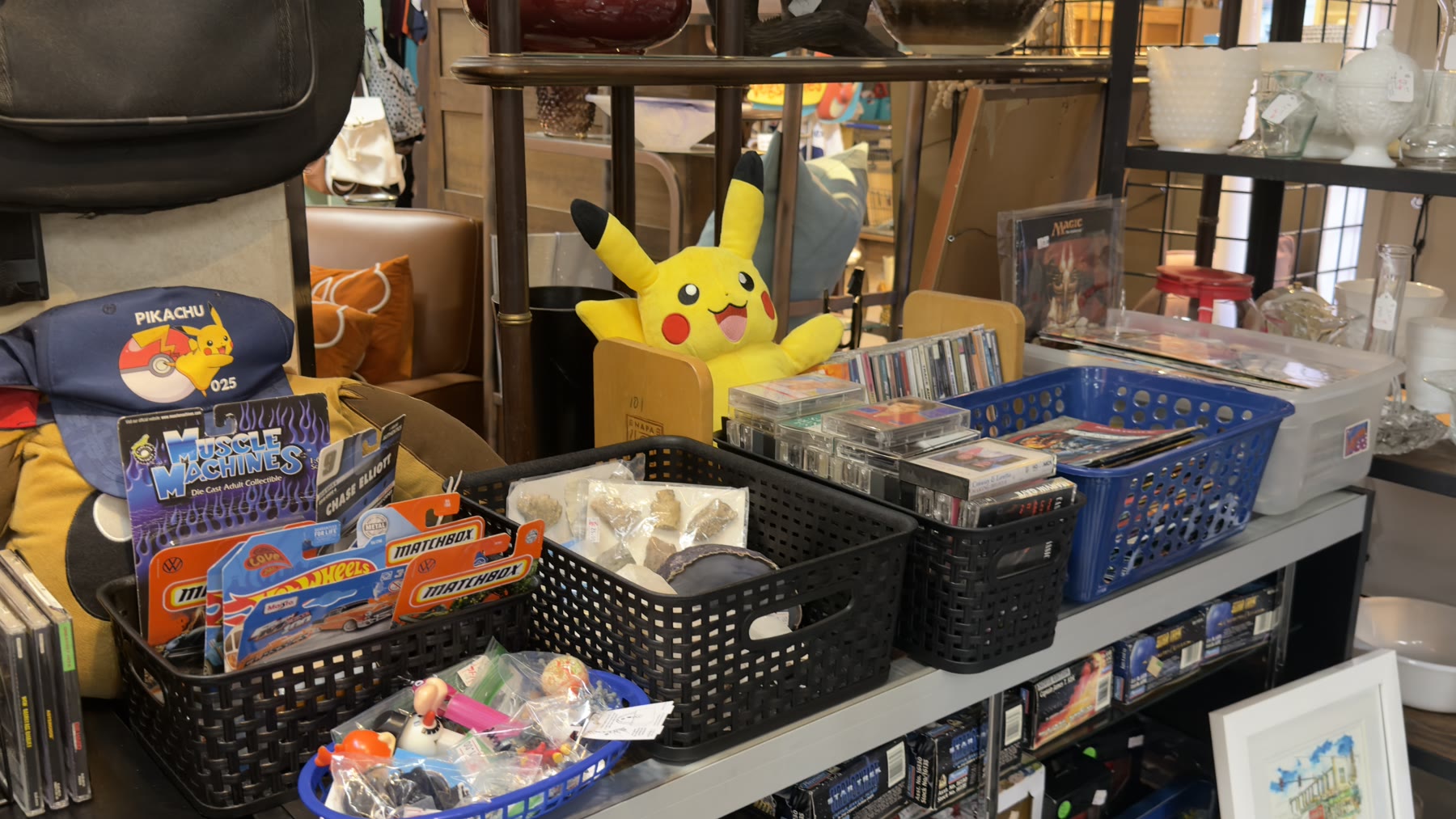 Pikachu plush, Hot Wheels, Matchbox cars, and Magic the Gathering cards on a vendor shelf